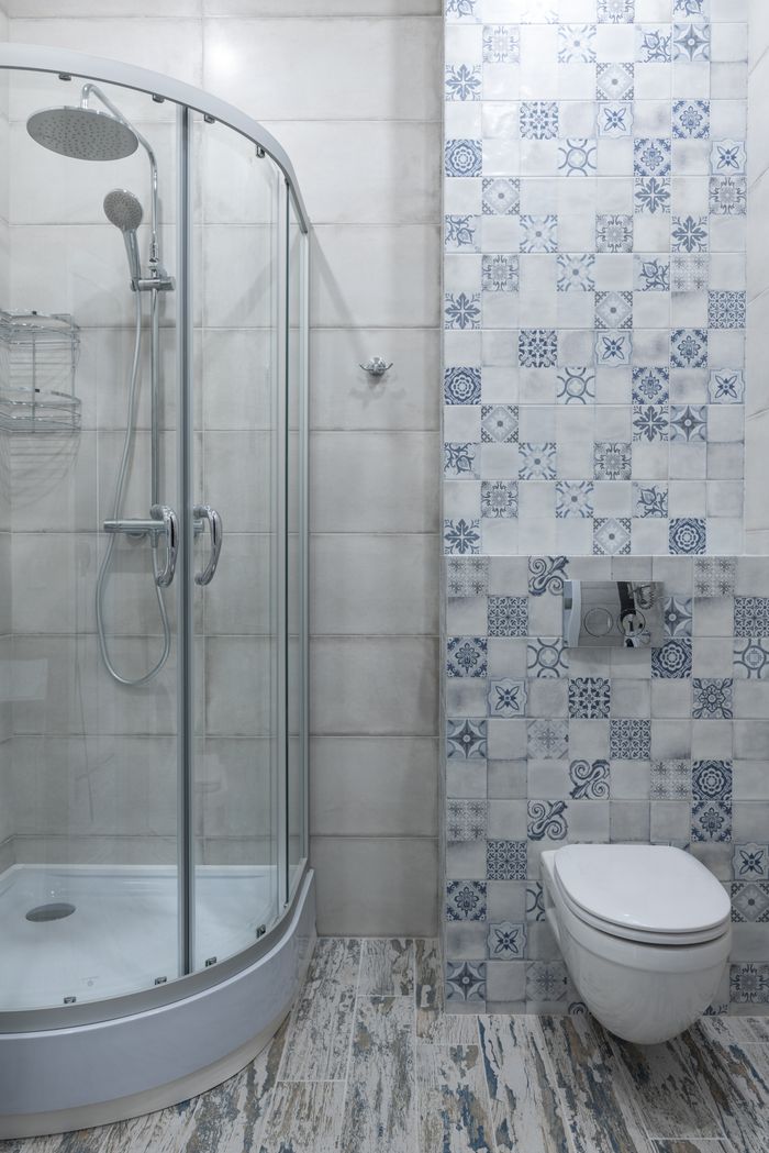 Interior of stylish bathroom with modern glass shower cabin placed near toilet at wall with ornamental tile in light room